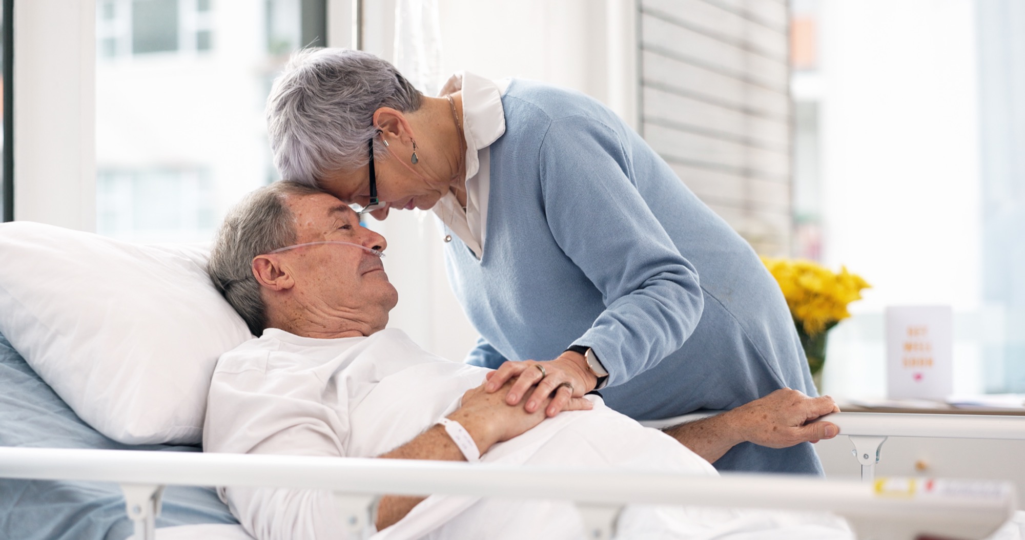 A caregiver lovingly comforts a resident in bed.