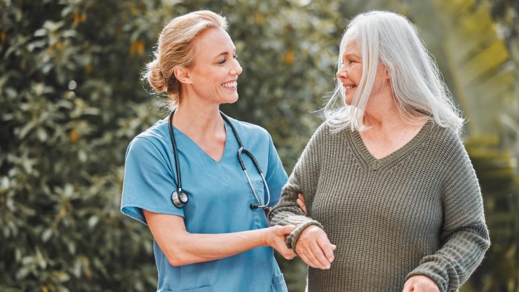 Nurse assisting an elderly woman outdoors.