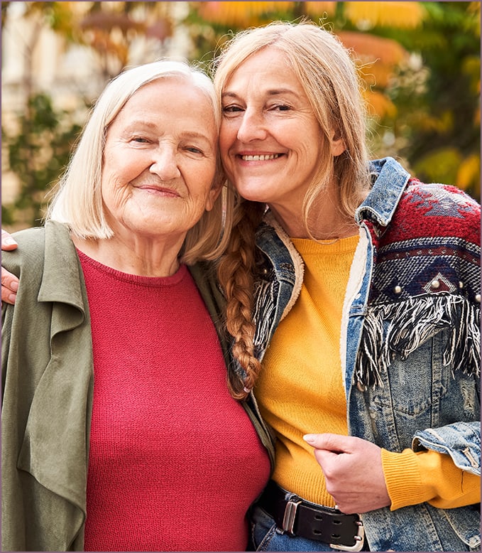 Two women smiling outdoors in a natural setting.