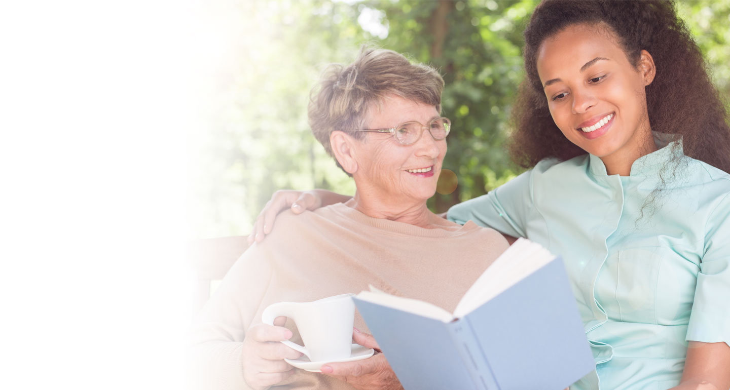 Senior resident reading with staff member outdoors