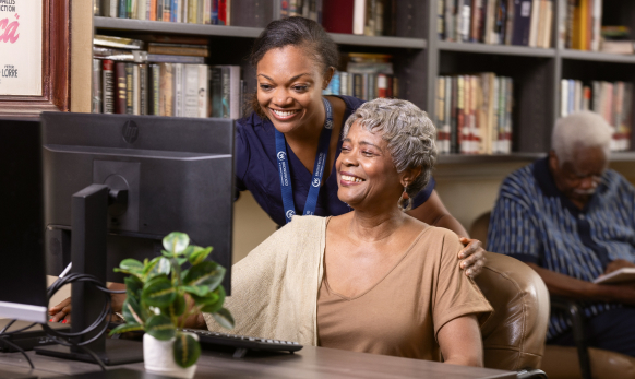 A staff member assisting an elderly resident at a computer.