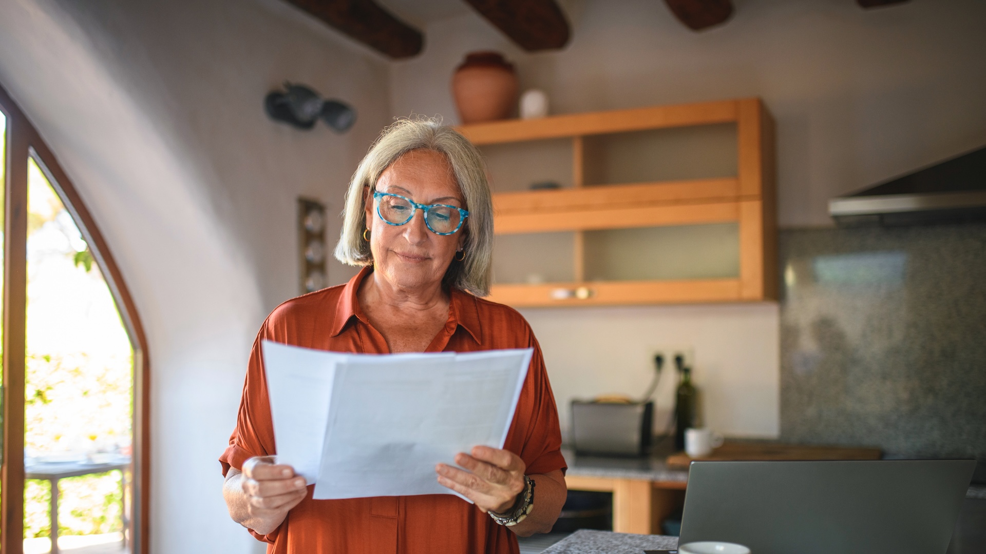 Older woman reading documents in a cozy kitchen