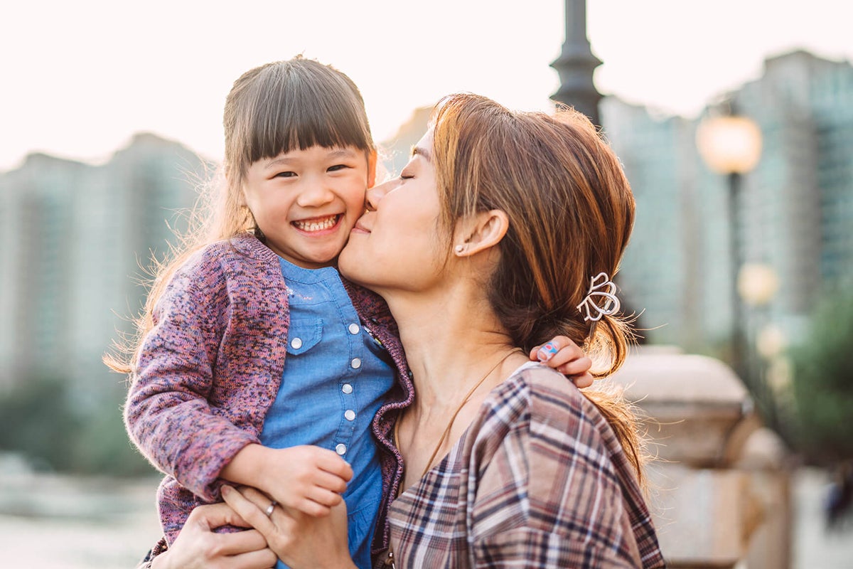 A woman kissing a girl outdoors, joyful moment.