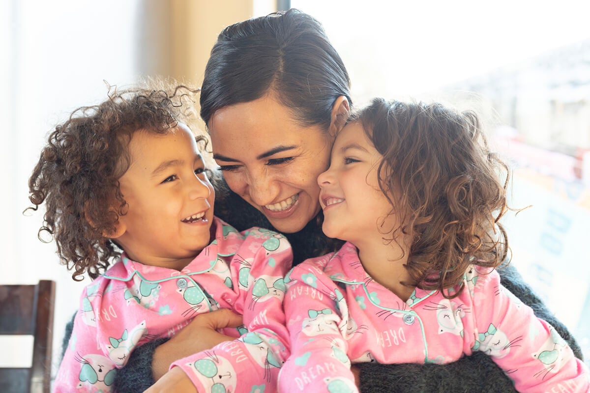A woman with two smiling children in pajamas
