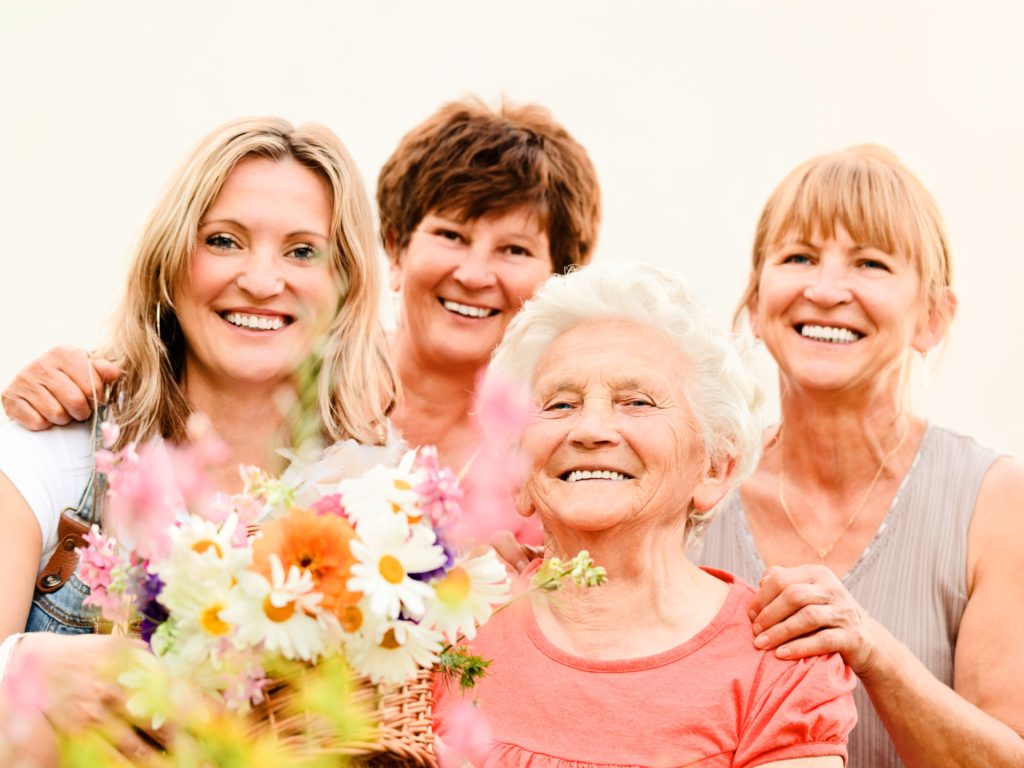 Four smiling women, one elderly resident with flowers