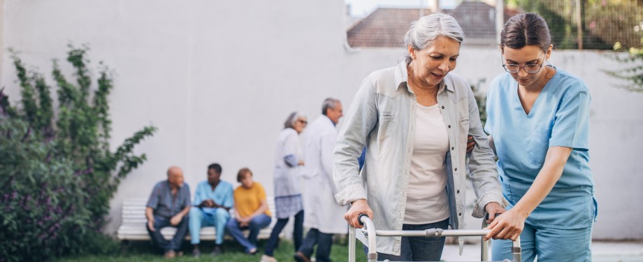Staff assisting a resident with a walker outdoors.