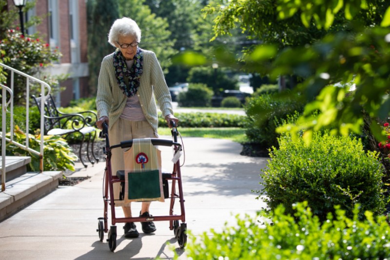 Elderly woman using a walker in landscaped garden
