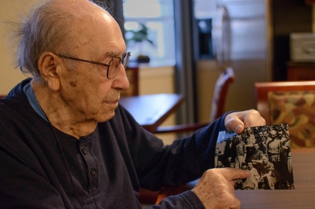 An elderly man holding a photograph in a common area.