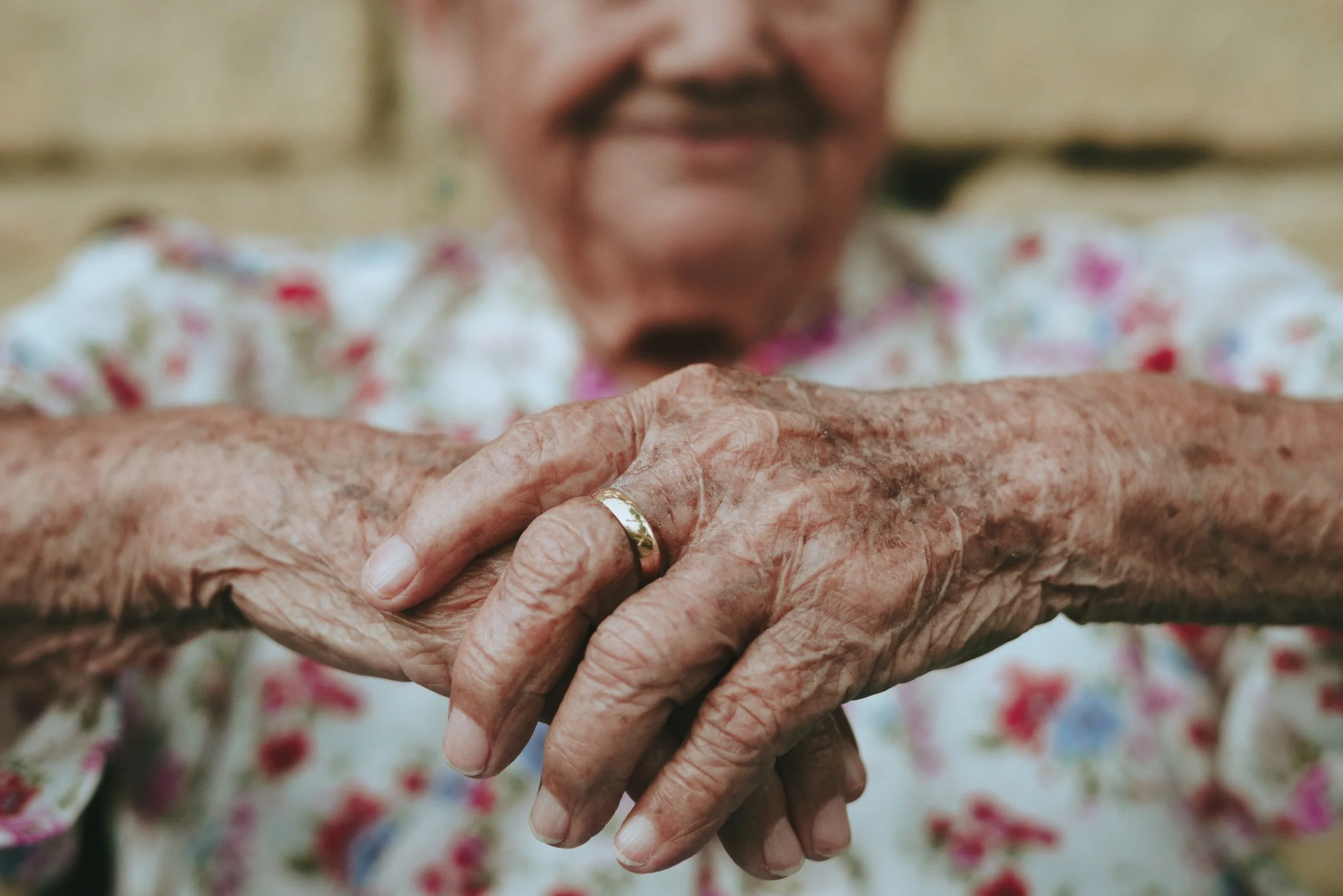 Elderly woman's hands with a ring resting on her lap.