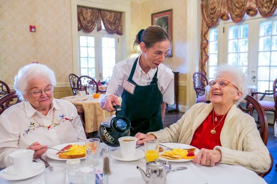 Two elderly women enjoying breakfast with a staff member.