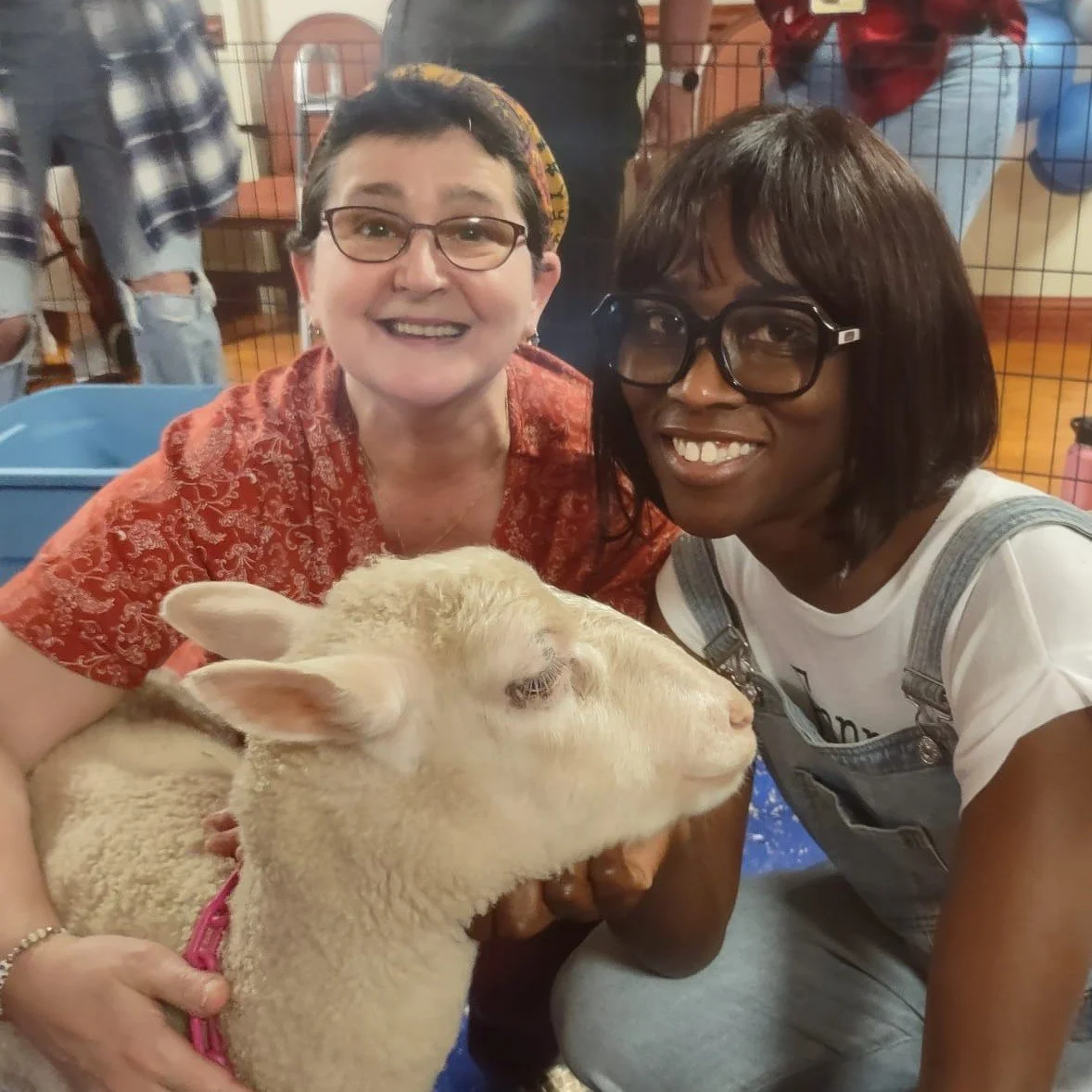 Two women smiling with a sheep in a care facility