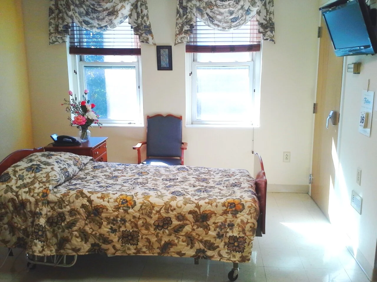 Cozy resident room with floral bedding and chair.