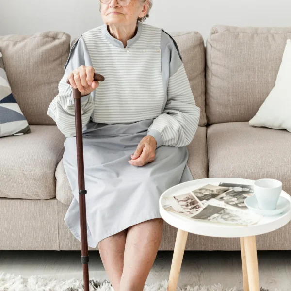 Senior woman seated with a cane in a living area.
