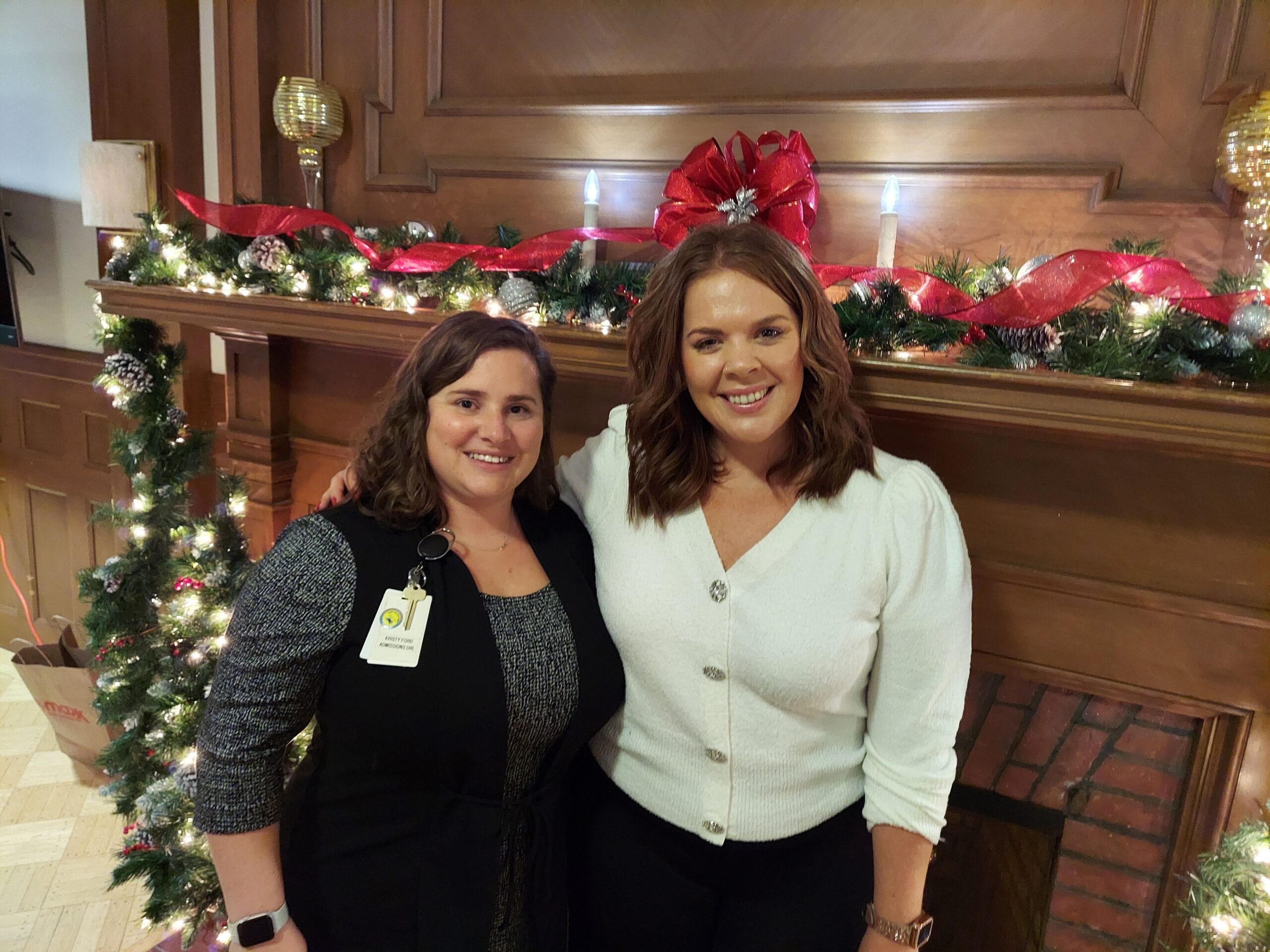 Two staff members smiling by a decorated fireplace.