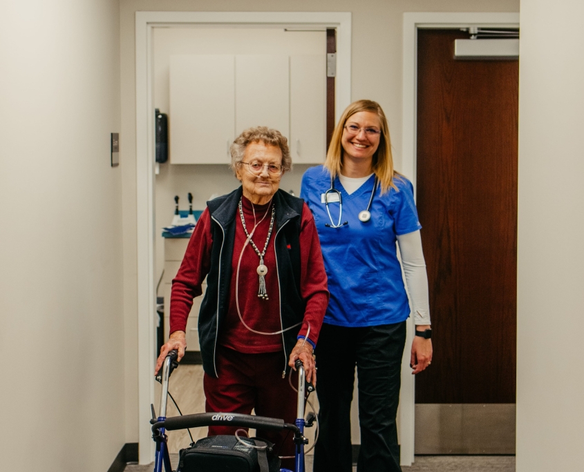 Elderly resident and staff member in a hallway.