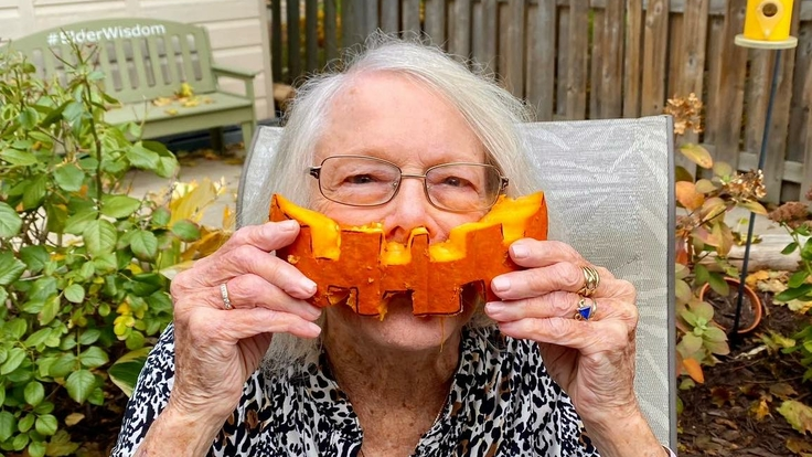 Elderly woman playfully holding a pumpkin slice.