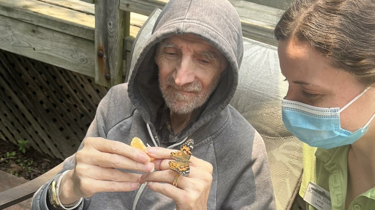 Senior man enjoying time outdoors with staff member and butterfly.