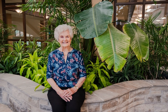 Senior woman smiling in a lush indoor garden setting.