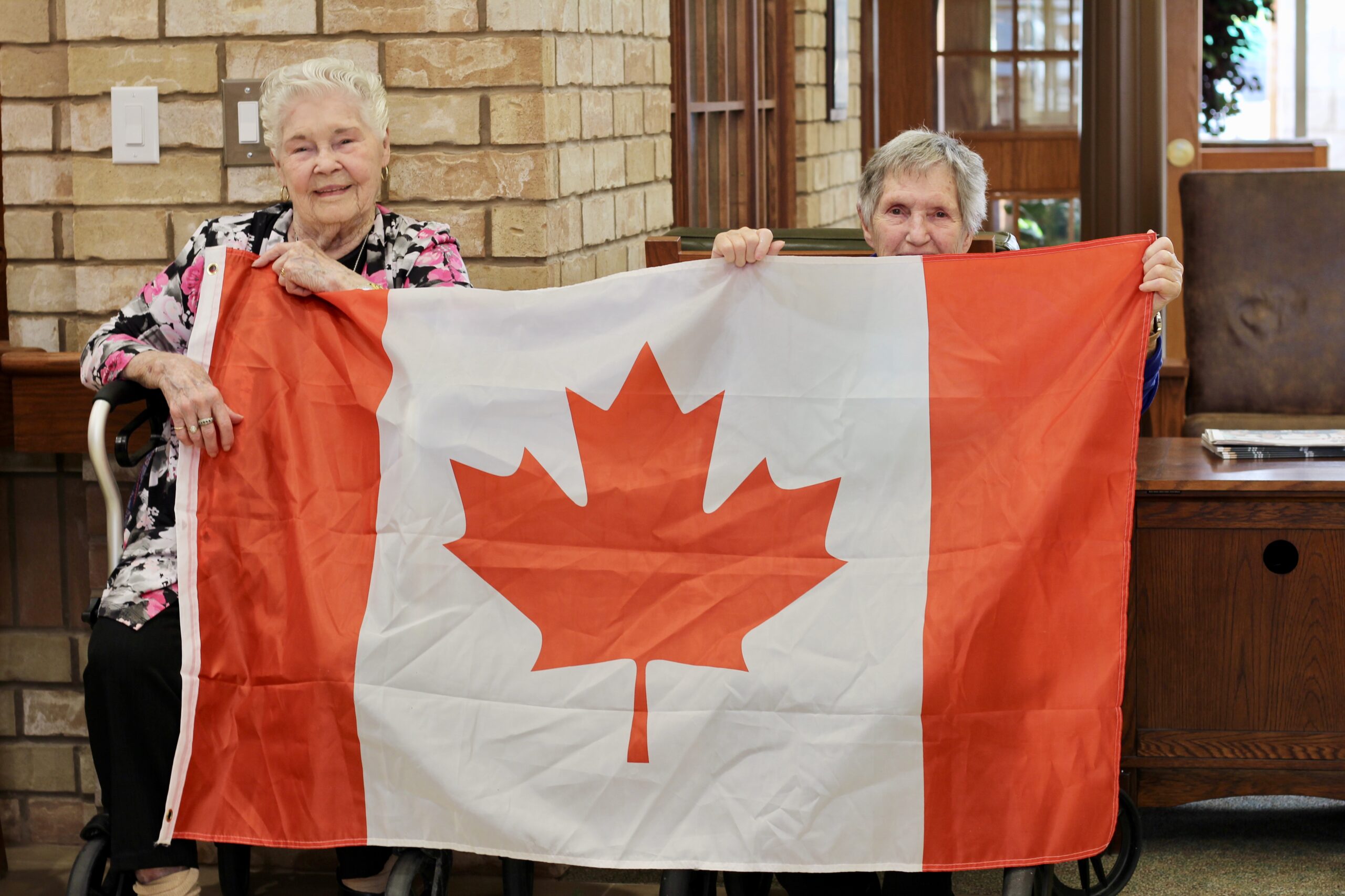Two women holding a Canadian flag indoors.