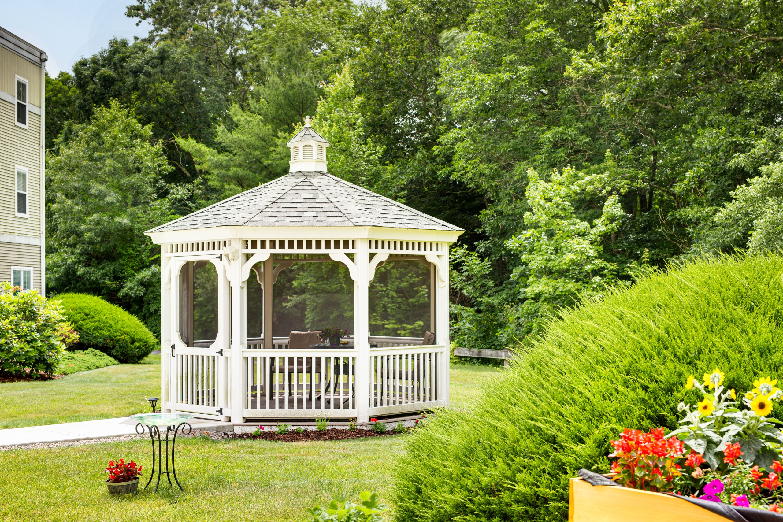 Outdoor gazebo surrounded by greenery and flowers.