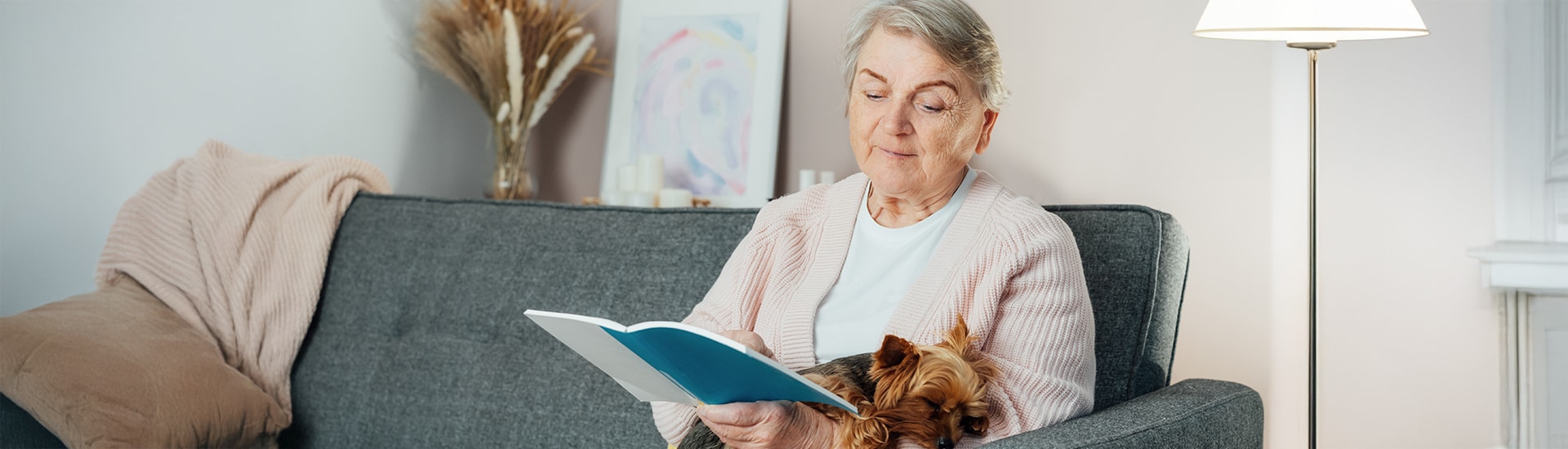 Senior woman reading on a couch with a dog.