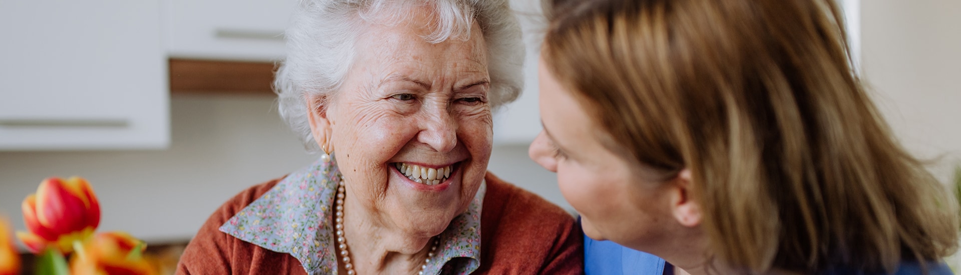 Caregiver smiling with elderly resident indoors.