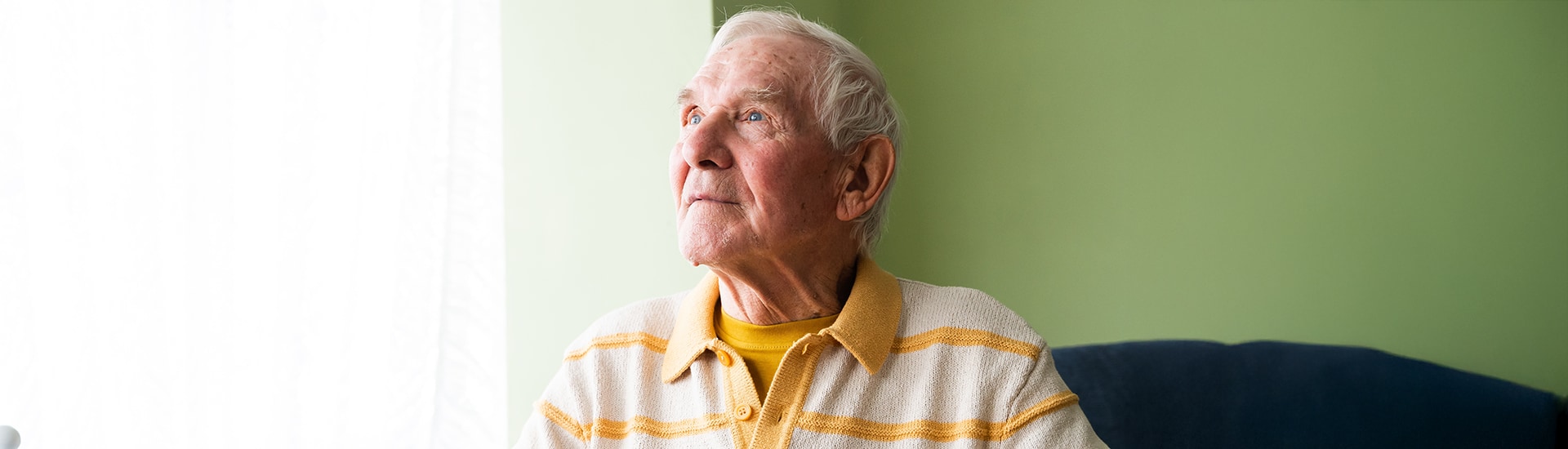 An elderly man looking out the window thoughtfully