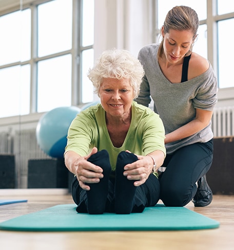 Senior woman stretching assisted by a staff member