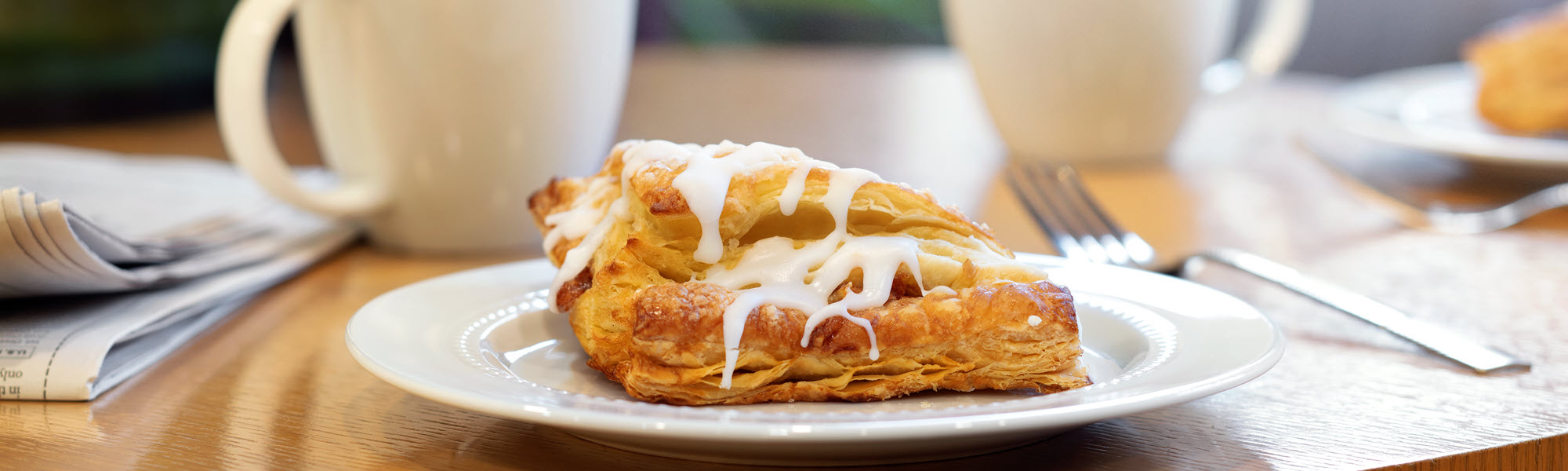 Plate of pastry with coffee cups in background.
