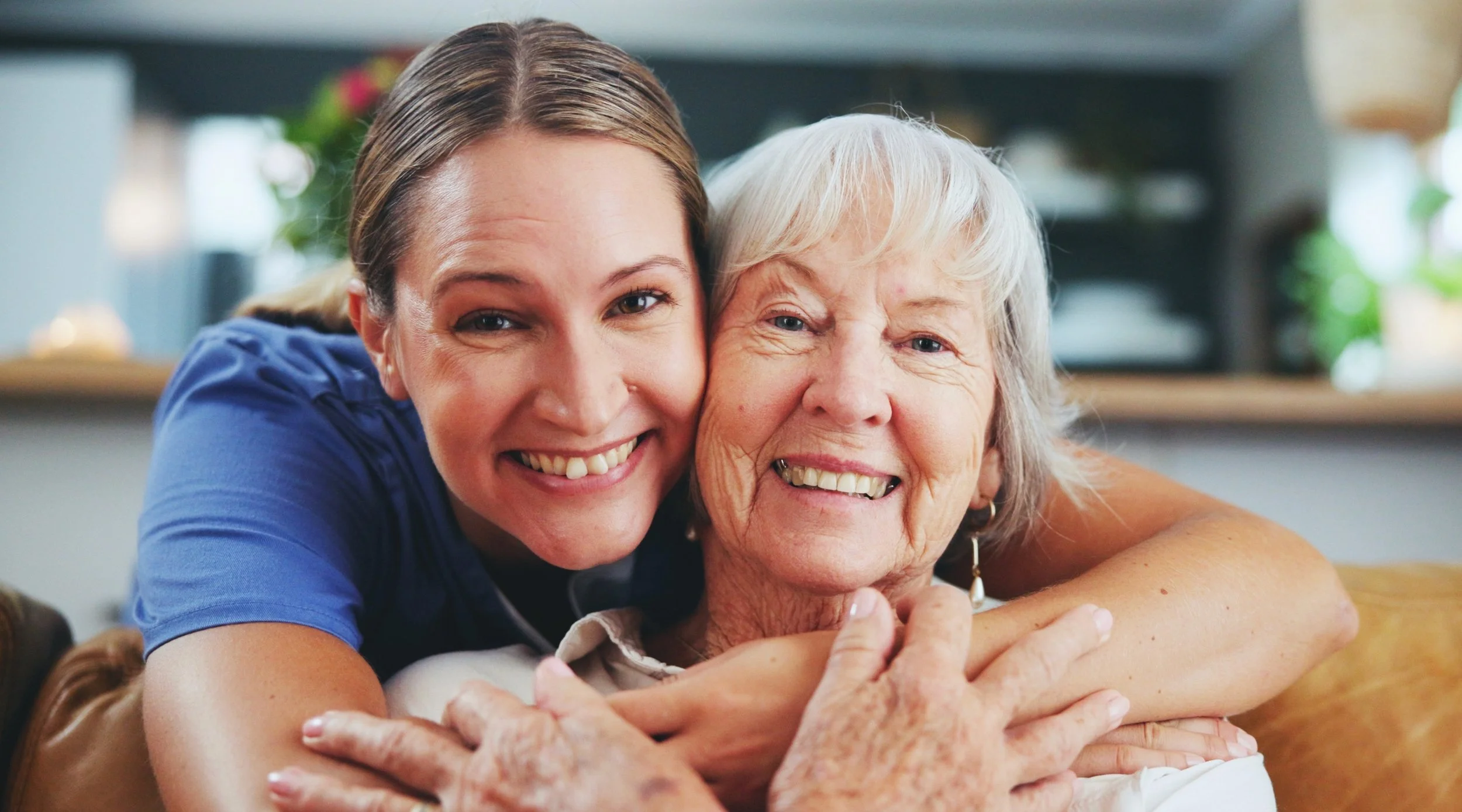 An elderly woman hugging a caregiver with smiles.