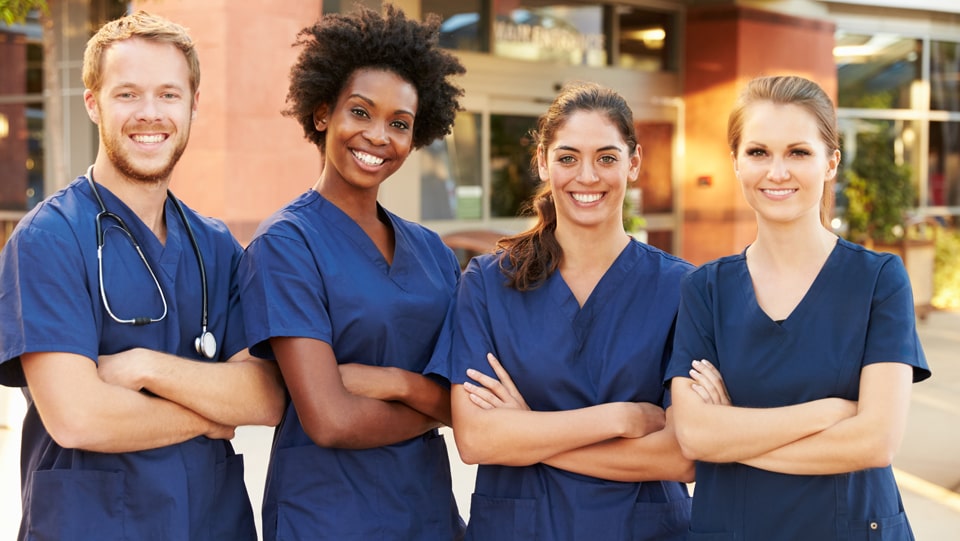Four healthcare professionals smiling outdoors.