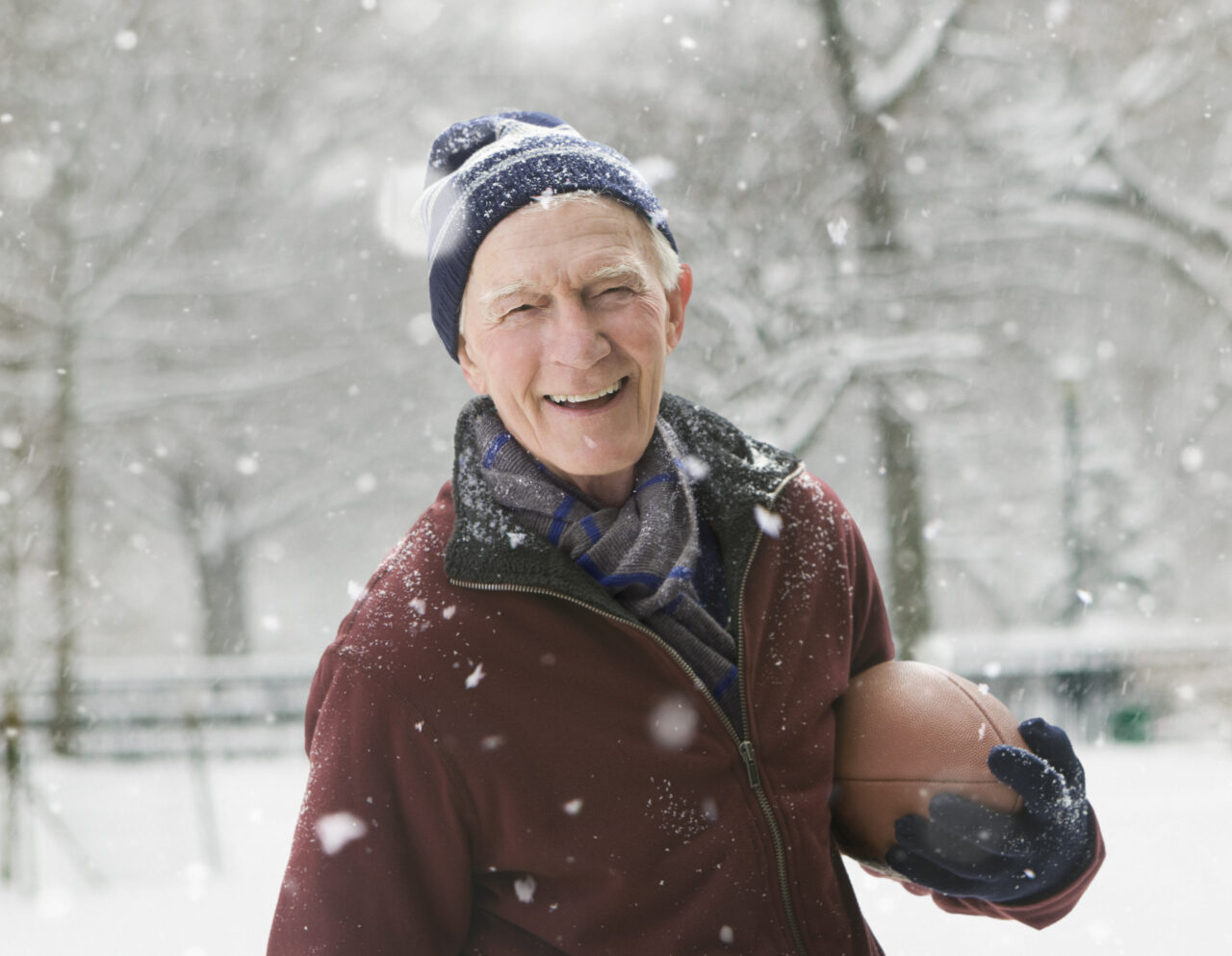 Senior man smiling with a football in the snow.