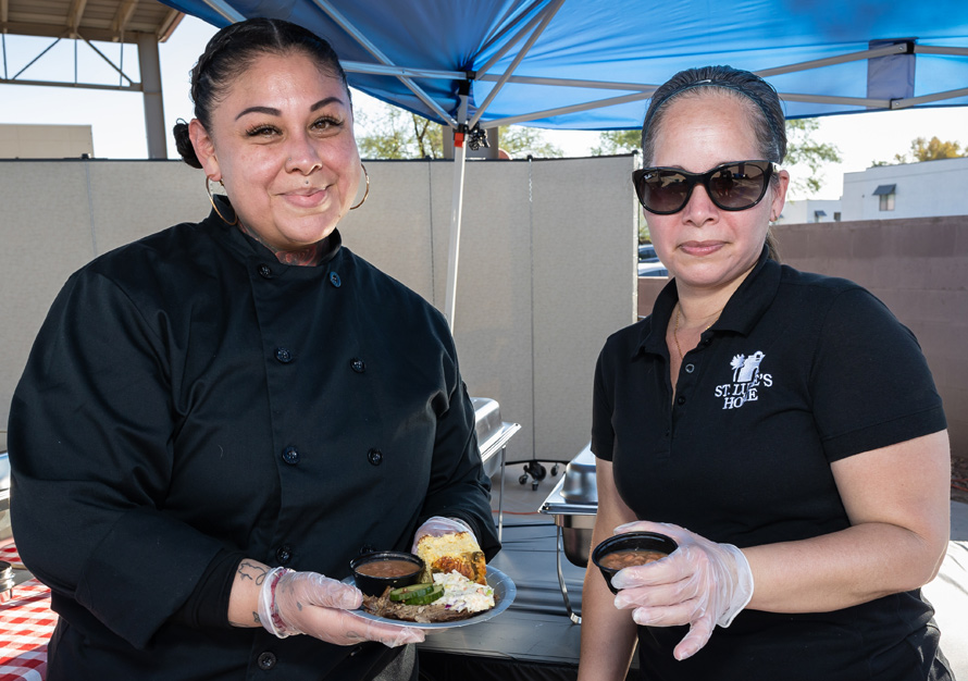 Two staff members serving food outdoors.