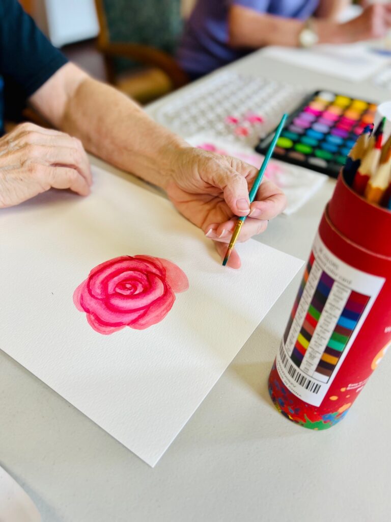 A person painting a pink rose with watercolors.