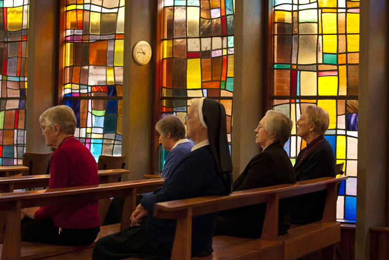 Residents praying in a chapel with stained glass windows.
