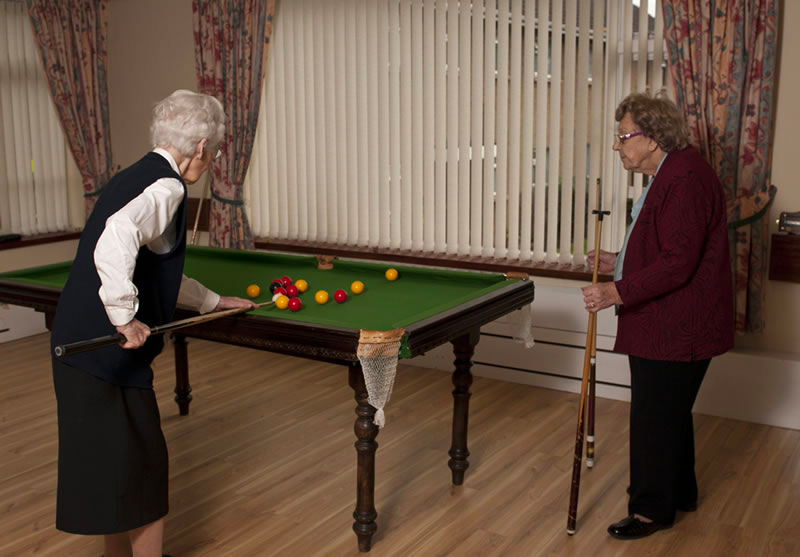 Two senior women playing billiards indoors.