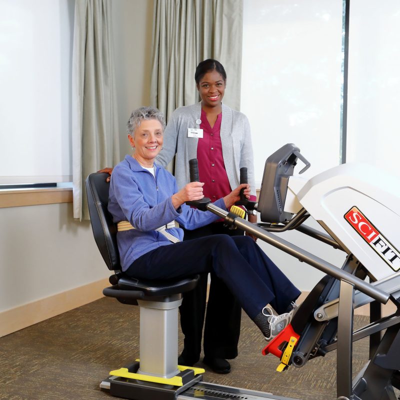Resident exercising with assistance in a facility gym.