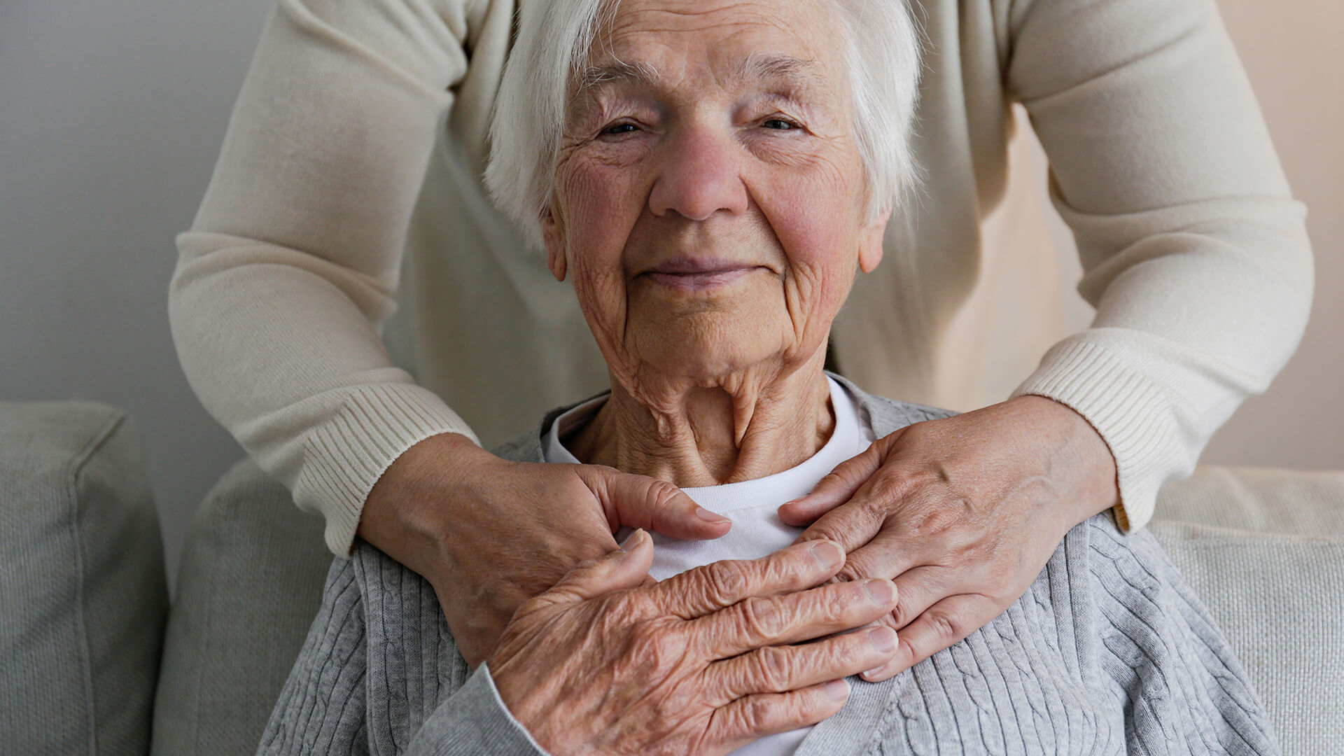 An elderly woman smiling with hands on her chest.