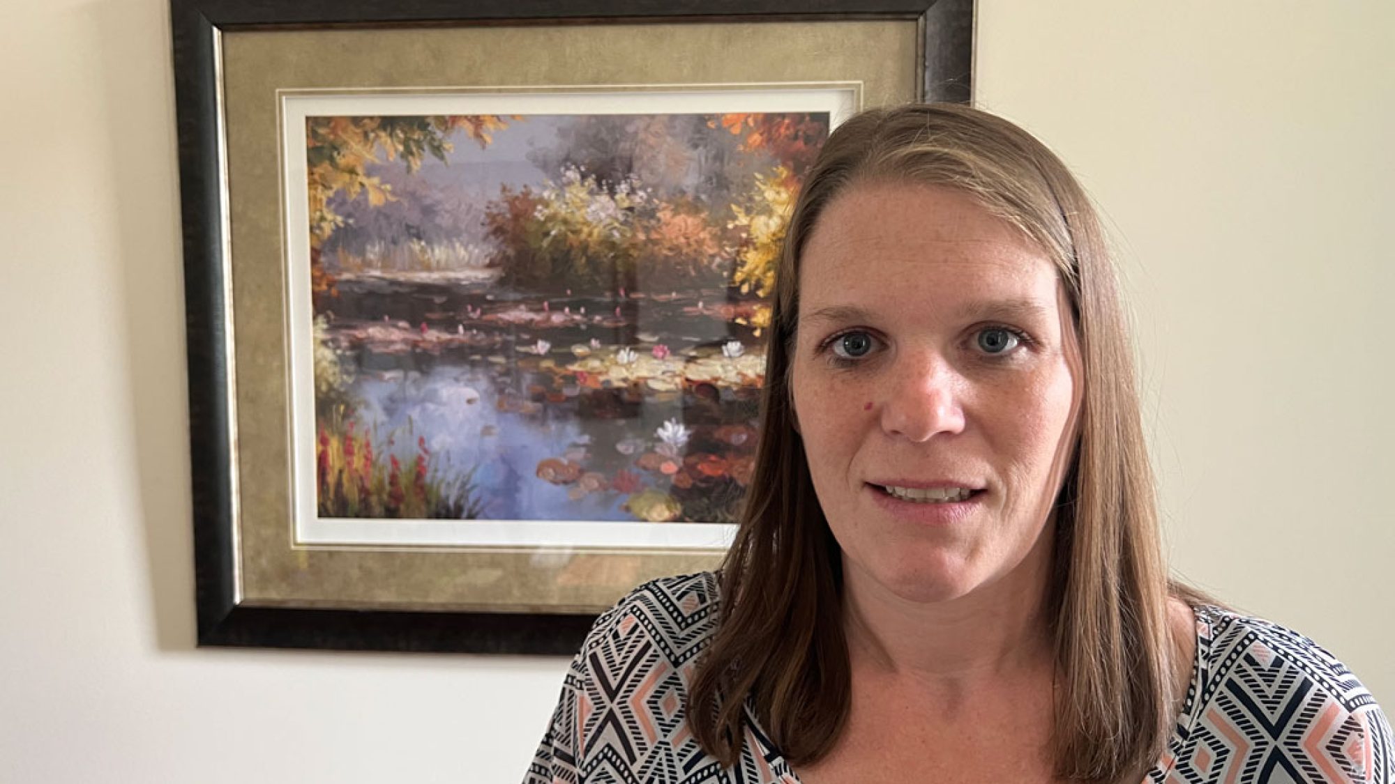 A woman in front of a nature painting.