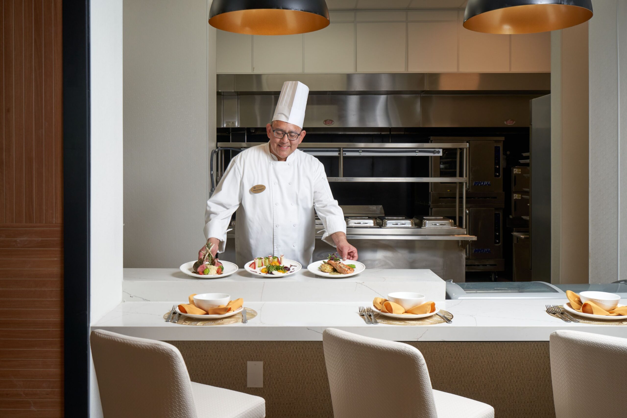 Chef presenting plated meals in a dining area.