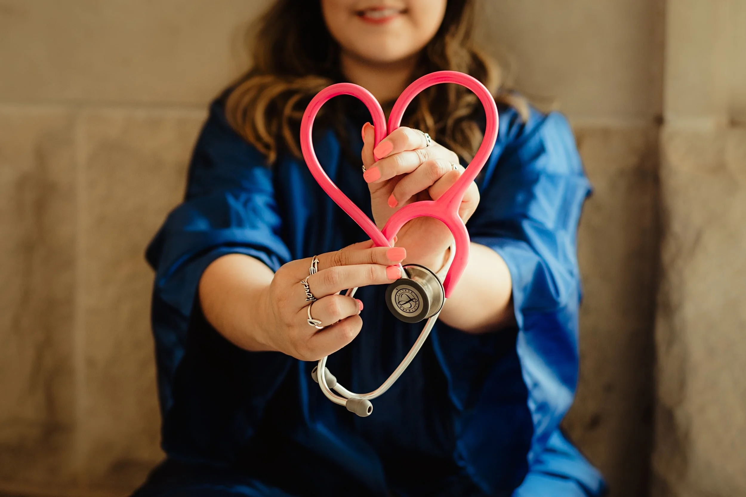 Person holding a pink stethoscope in a heart shape.