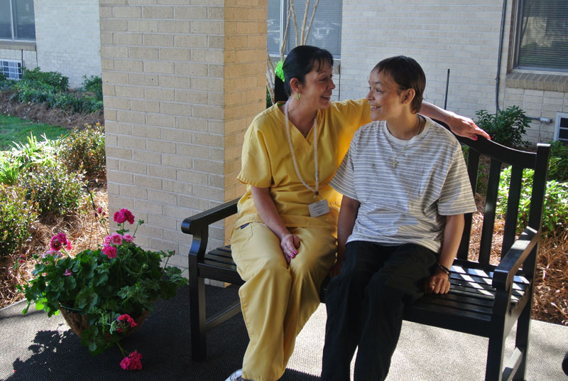 Staff member and resident smiling on a bench outside.