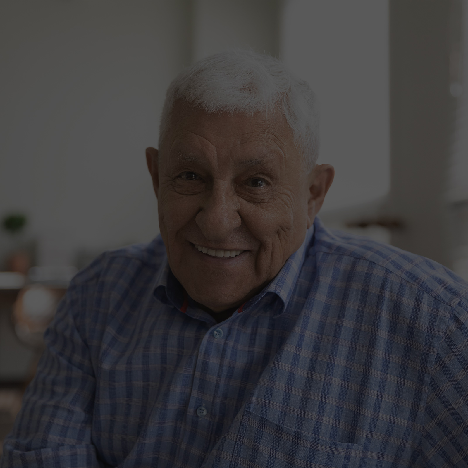Smiling elderly man in a checkered shirt.