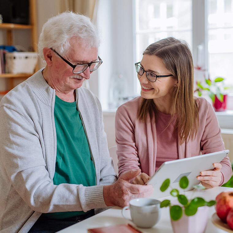 A caregiver assisting a senior man with a tablet