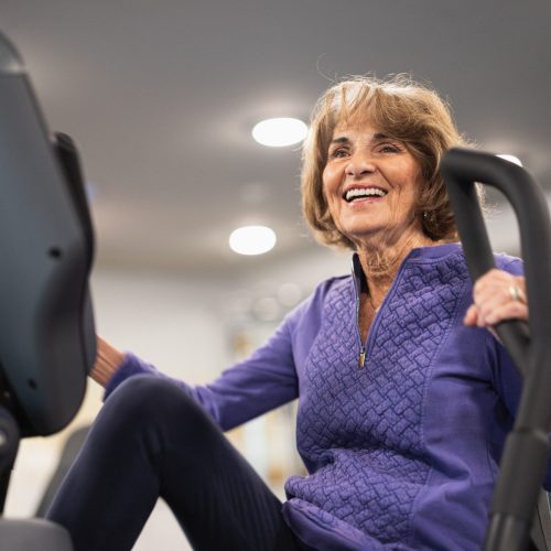 A senior woman exercising on a machine, smiling.