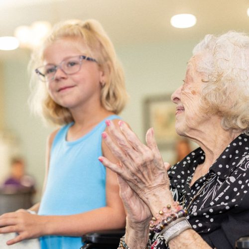 A young girl interacting with an elderly woman, both smiling