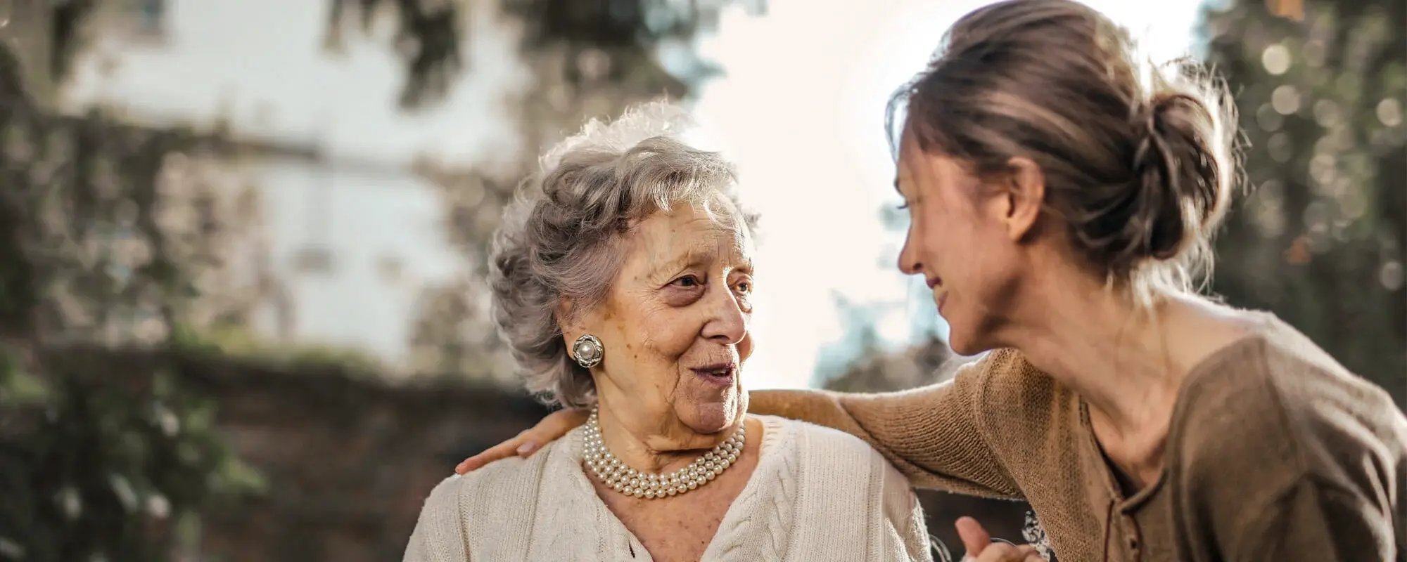 An elderly woman sharing a joyful moment with a staff member outdoors