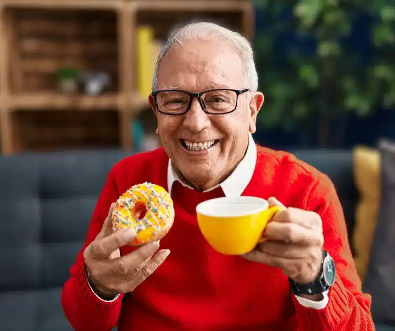 Happy senior enjoying a donut and tea in a cozy setting
