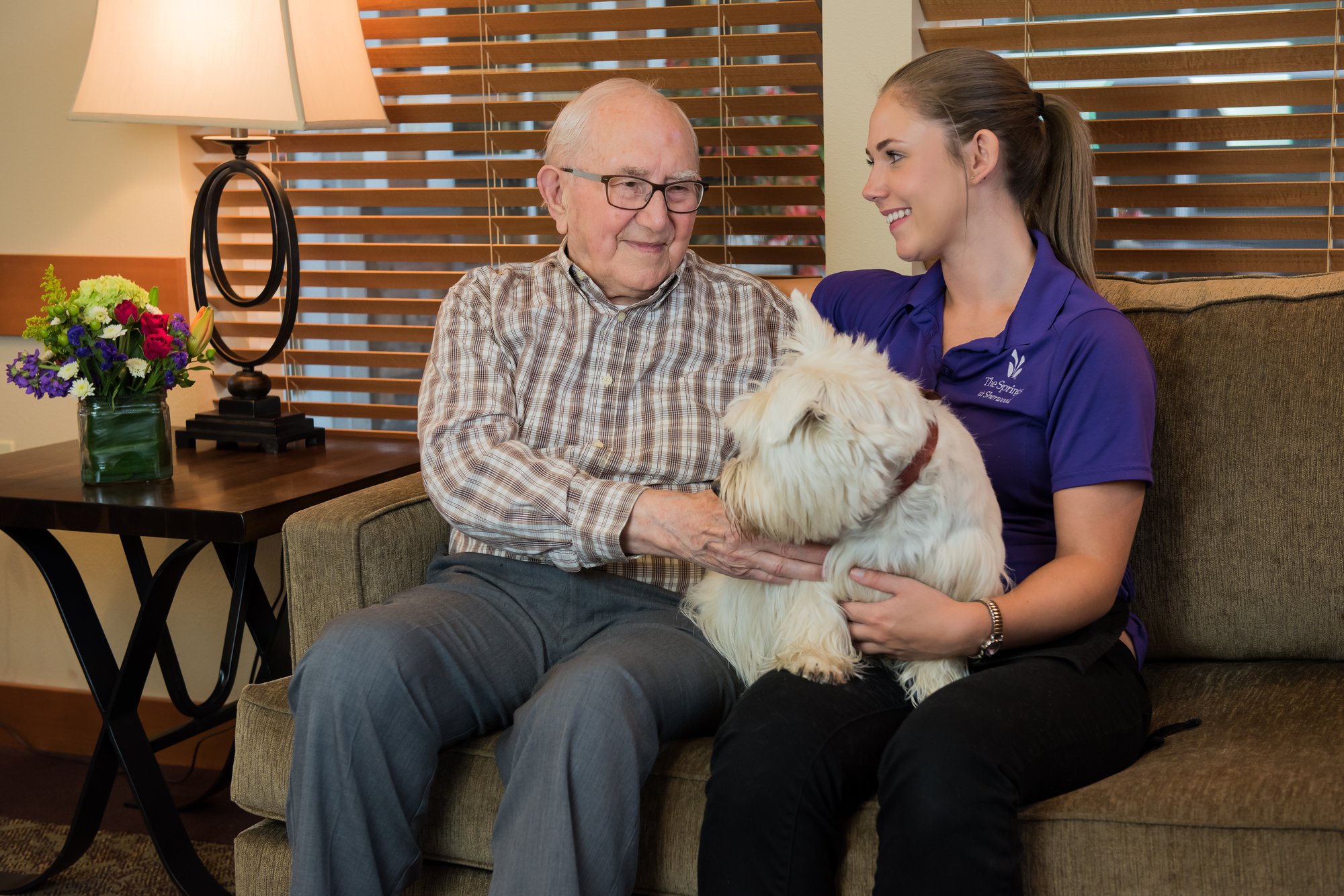 A caregiver with a resident and a dog in a cozy living room