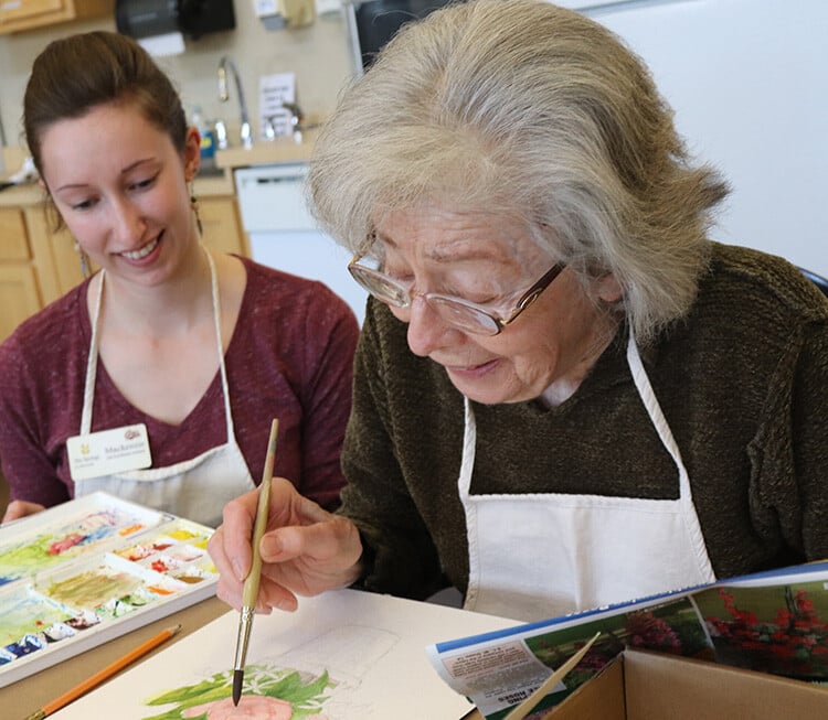 Resident painting with staff assistance in an indoor activity